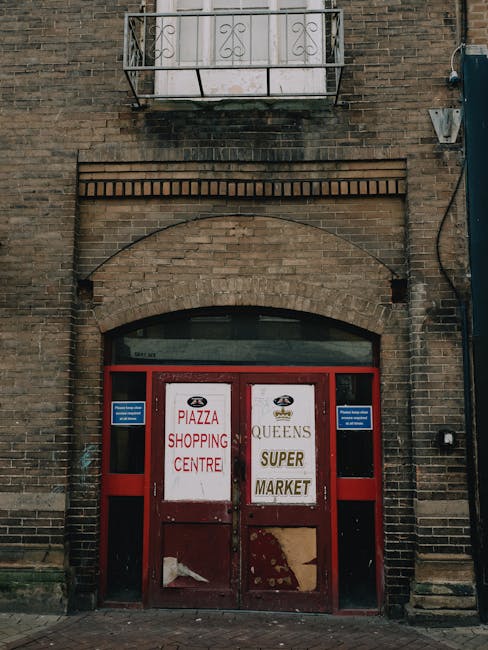 A city street scene featuring the exterior of a brown-painted bar and restaurant with large windows and a sign indicating it serves wines, spirits, and oysters, situated on Crispin Street. In front of the establishment, a large black commercial waste bin designated for waste only is positioned on the sidewalk, filled with flattened cardboard boxes and paper debris. The bin has visible white text and contact details, indicating its use for waste collection purposes by Waste Collection Barnet. To the left of the bin, a black bollard stands, and next to it on the ground, a few discarded sheets of paper or cardboard are scattered. Across the street, a blue truck is parked, and a bicycle is secured to a nearby bike rack. The road features a clearly marked circular parking restriction sign painted on the tarmac, while a lamppost and additional bicycles are visible in the background, along with neighboring brick buildings, suggesting an urban environment with provisions for private waste disposal and alternative rubbish removal services.